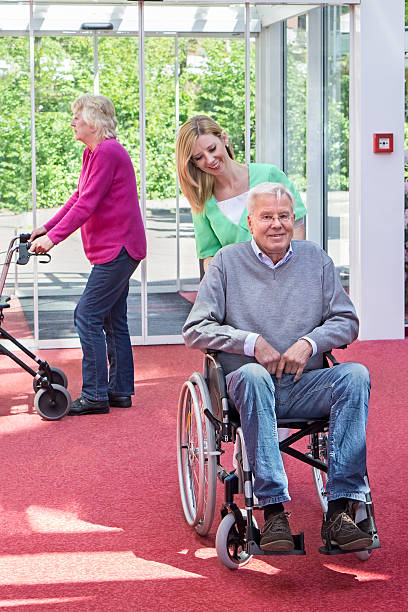 istock Nurse Pushing Senior Man in Wheelchair, Nursing Home Lobby. 480802454