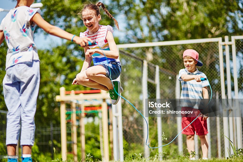 Happy jumping Happy girl jumping over skipping-rope held by her friends outdoors Jump Rope Stock Photo