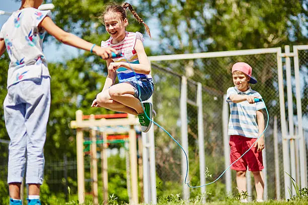Happy girl jumping over skipping-rope held by her friends outdoors