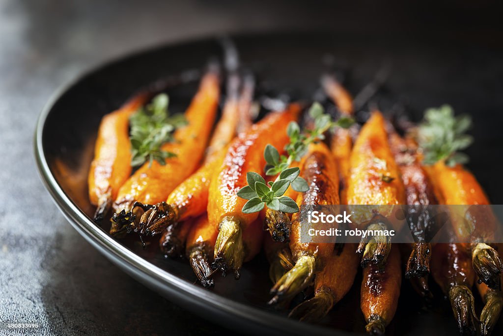 Baked Baby Carrots with Thyme Oven baked baby carrots with thyme, in black plate over slate. Carrot Stock Photo