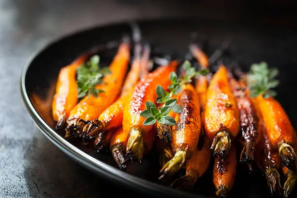 Oven baked baby carrots with thyme, in black plate over slate.