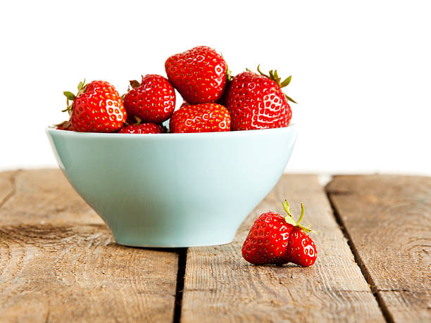 Sorted out Misshaped strawberry in front of bowl with perfect fruit on wooden crate, white background misshaped stock pictures, royalty-free photos & images