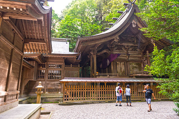 Takachiho, Japan - August 7, 2014: View on wooden shrine surrounded with cedars, three tourist standing in front of it and taking photos. 
