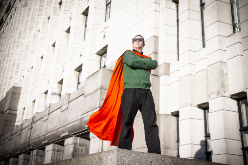 Caped geek superhero stands on pedestal surveying the city he protects.