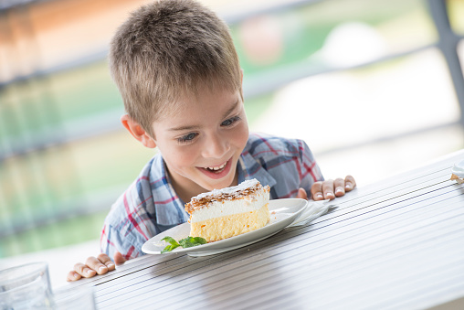 Little boy making faces. He is happy to have a creamcake. Outdoors, on a terrace of a restaurant.
