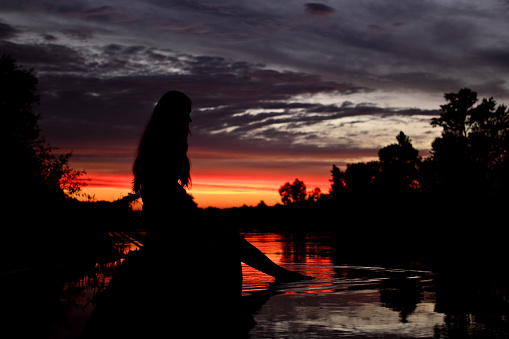 Silhouette of the girl at the river at sunset