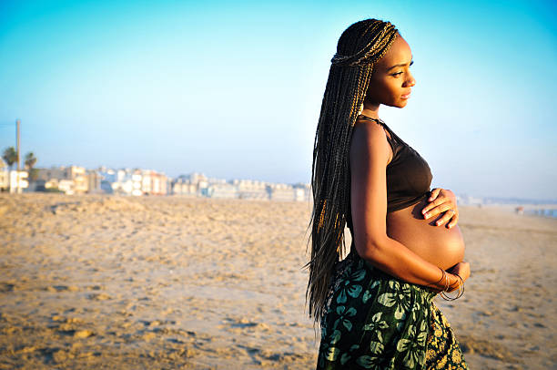 A pregnant woman holds her belly and stares into at the ocean. Horizontla image with copy space. Shot in natural light at Venice Beach CA. 