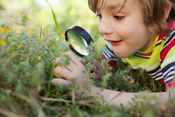 felice piccolo bambino guardando attraverso la lente d'ingrandimento - searching child curiosity discovery foto e immagini stock