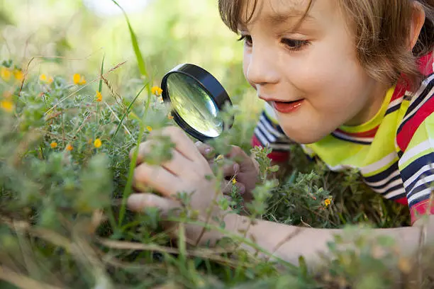 Photo of Happy little boy looking through magnifying glass