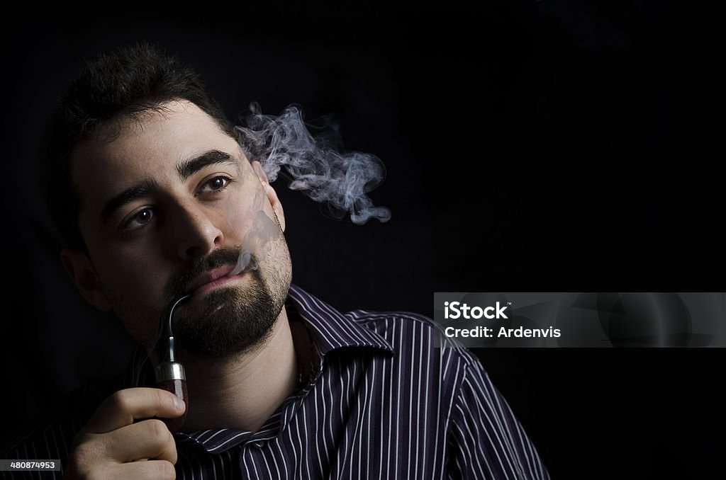 Giovane Barbuto uomo fumo un tubo su sfondo nero - Foto stock royalty-free di Adulto