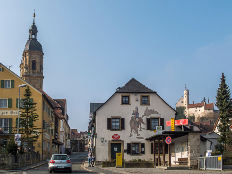 Gössweinstein, Germany - March 6, 2014: Pedestrians and cars in Gößweinstein in the Franconian Switzerland. Left the basilica and on the right in the background the castle Gößweinstein.