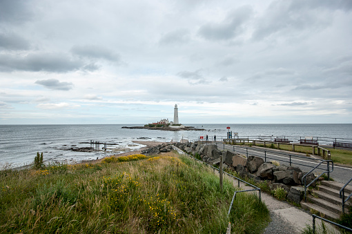 A shot of St Mary's Island, on which stands St Mary's Lighthouse.  Taken from the shore, with the tide in, and thick clouds in the sky.