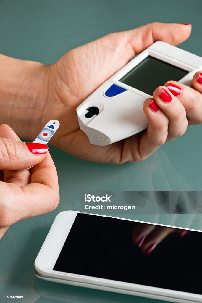 Personal blood sugar test Personal blood sugar test with blood sugar meter and smart phone. Diabetes patient checking glucose levels, using smart phone to keep track of it. Blood sugar meter, smart phone, test strip, hand 2015 Stock Photo