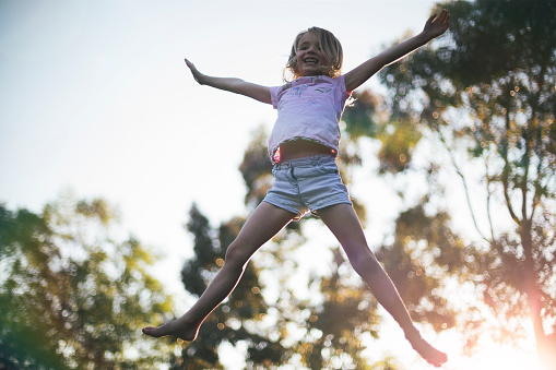 Backlit image of a little girl bouncing on a trampoline at sunset.