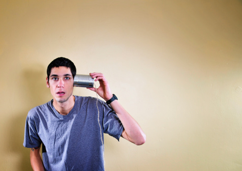 A young man holds a toy can-phone to his ear as he listens and zones out. Horizontal image shot with a lot of copy space.