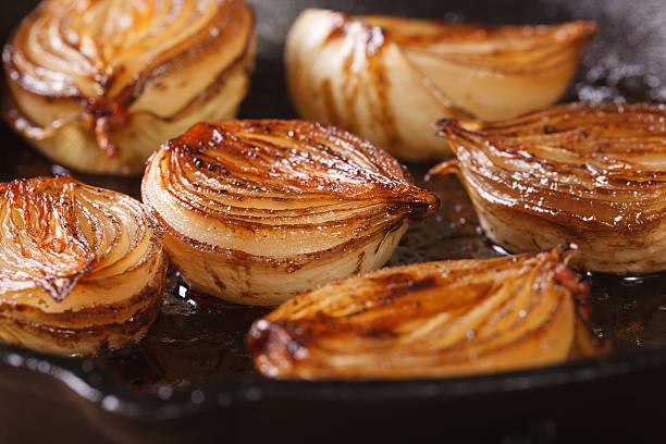 oignon ñaramelized moitiés avec vinaigre balsamique dans une poêle - oignon photos et images de collection