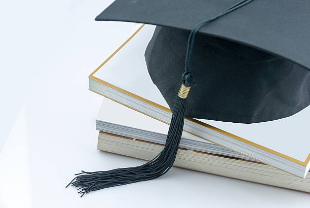 mortarboard on a book stack on white background a mortarboard on a book stack on white background. icon image for costs in training and education dissertation photos stock pictures, royalty-free photos & images
