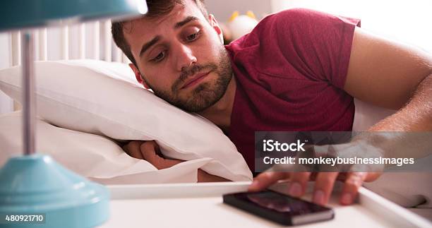 Man In Bed Woken By Alarm On Mobile Phone Stock Photo - Download Image Now - Alarm Clock, Urgency, Waking up