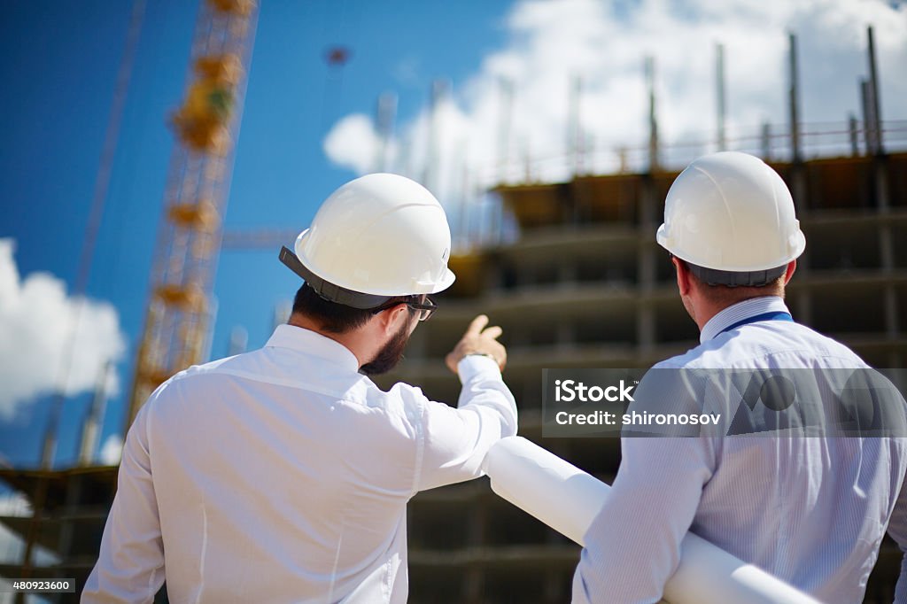 Showing building construction Rear view of architects looking at construction while one of them showing it to colleague Construction Worker Stock Photo