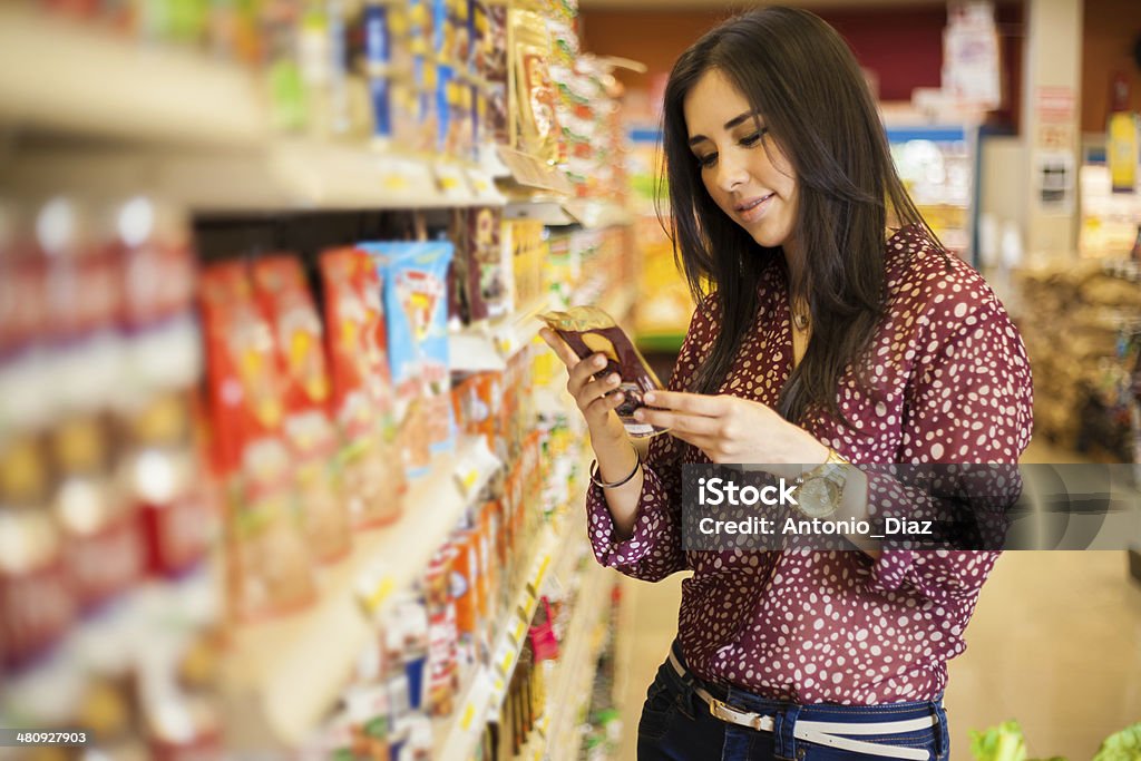 Looking at the food label Cute young woman examining a product label while shopping at the store Label Stock Photo