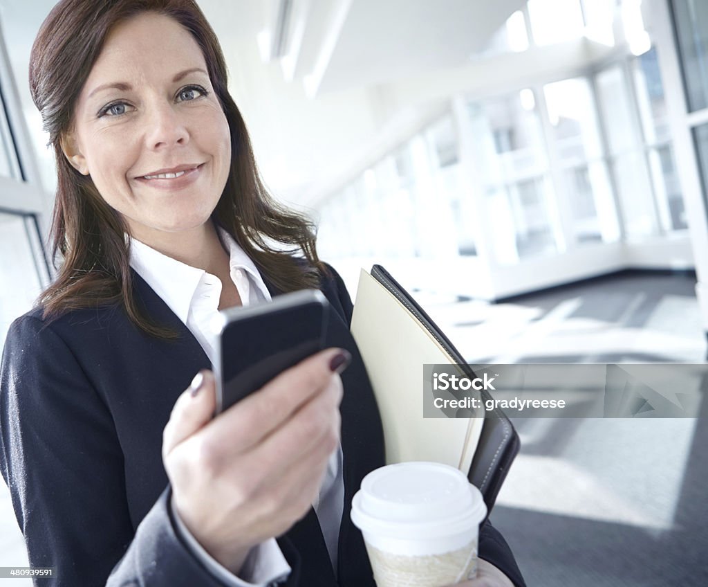 She's an excellent multi-tasker! An attractive businesswoman checking her mobile in the corridor at work 30-39 Years Stock Photo
