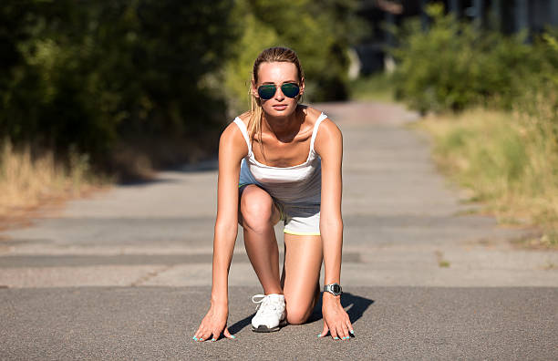 Silhouette of a woman tying her shoelace in the park. She is exercising an about to go running at sunset or sunrise with the city of Sydney in the background. Focus on background. Copy space