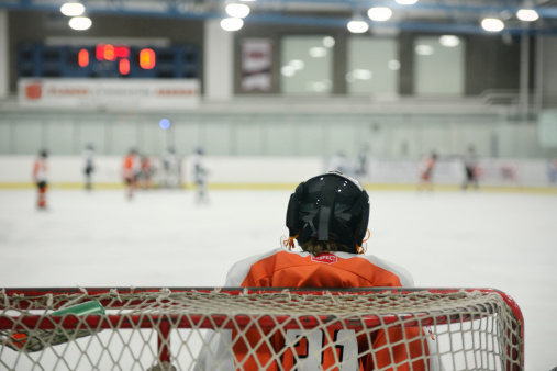 Child hockey goalie in net facing opposition on ice rink