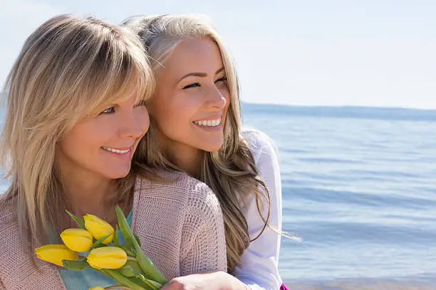 happy mother and daughter with flowers relaxing on the beach