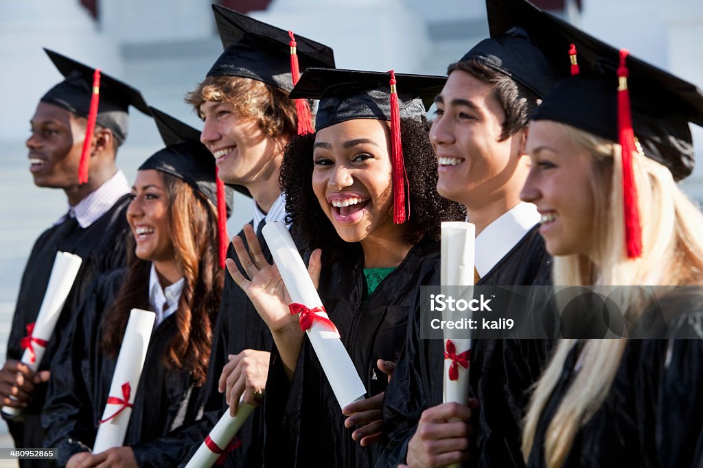 Graduating class Multi-ethnic friends graduating together, in cap and gown.   Main focus on African American girl in middle, waving at camera. Graduation Stock Photo
