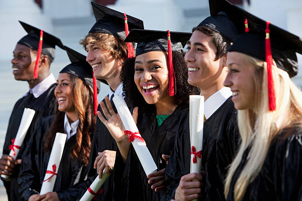 Graduating class Multi-ethnic friends graduating together, in cap and gown.   Main focus on African American girl in middle, waving at camera. mortarboard photos stock pictures, royalty-free photos & images