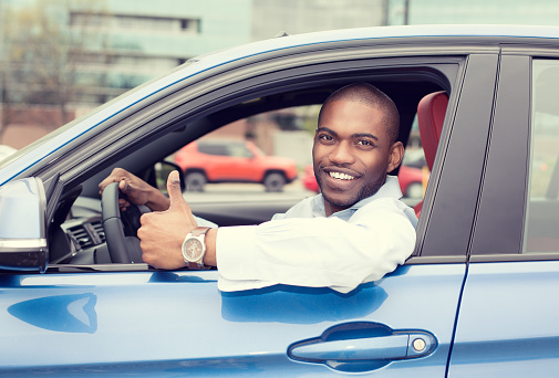 Car side window. Man driver happy smiling showing thumbs up driving sport blue car isolated outside parking lot background. Handsome young man excited about his new vehicle. Positive face expression
