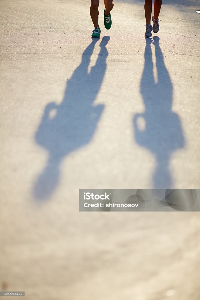 Running down asphalt road Two pairs of legs in sports-shoes and shadows of couple on asphalt road 2015 Stock Photo