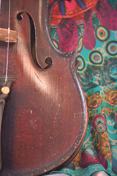 Antique violin closeup against quirky fabric print Closeup of a violin against a bright, artsy fabric background. Violin is an antique from the early 1800's in a dark stain (original finish). Vertical orientation. violin f hole stock pictures, royalty-free photos & images