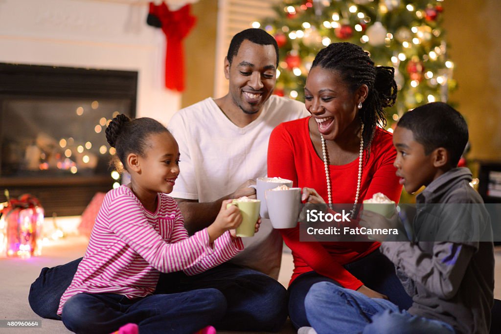 Family Gathered on Christmas Morning An African American family of four sharing hot cocoa on Christmas morning in the family living room next to the Christmas tree. Family Stock Photo