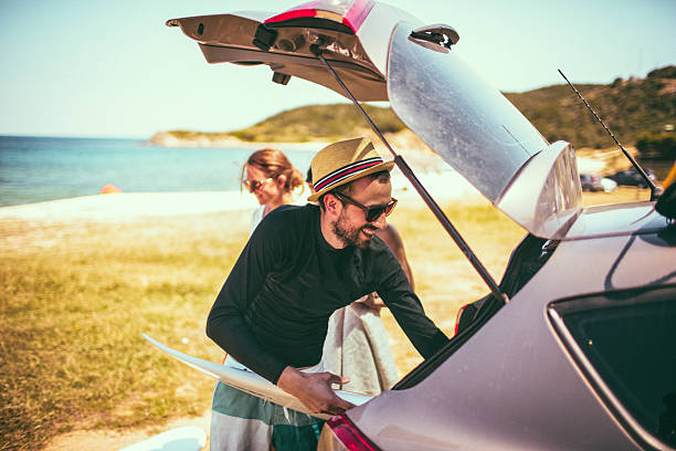 Summer trip Photo of smiling young people on a road trip, packing their car trunk at the beach hipster car stock pictures, royalty-free photos & images
