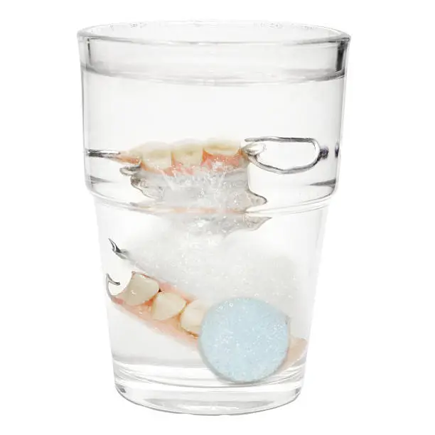 False Teeth in a glass with cleaning tablets and water glass "isolated on white"
