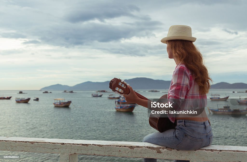 beautiful red-haired girl with a guitar beautiful red-haired girl sitting on a fence with a guitar on the beach 2015 Stock Photo