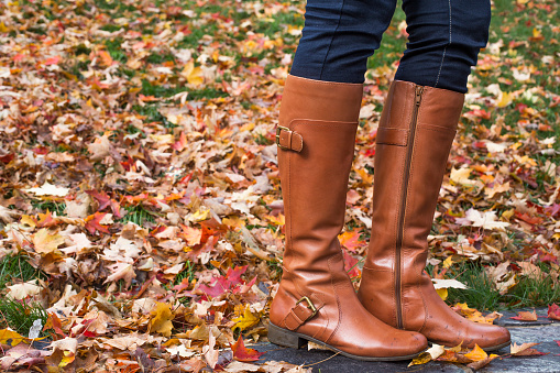 Unrecognizable woman wearing brown boot  and standing on foliage