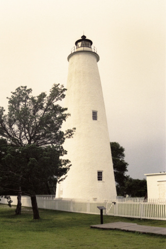 The Ocracoke Lighthouse, built in 1823, stands on Ocracoke Island, N. Carolina & is about 75 feet tall with a diameter narrowing from 25 feet at the base to 12 feet at its peak. The walls are five feet of solid brick at the base and tapering to two feet at the top. An octagonal lantern crowns the tower and houses the light beacon of a Fresnel lens with its hand-cut prisms and magnifying glass.