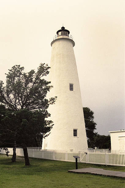 Retro Ocracoke Light Station The Ocracoke Lighthouse, built in 1823, stands on Ocracoke Island, N. Carolina & is about 75 feet tall with a diameter narrowing from 25 feet at the base to 12 feet at its peak. The walls are five feet of solid brick at the base and tapering to two feet at the top. An octagonal lantern crowns the tower and houses the light beacon of a Fresnel lens with its hand-cut prisms and magnifying glass. ocracoke island stock pictures, royalty-free photos & images