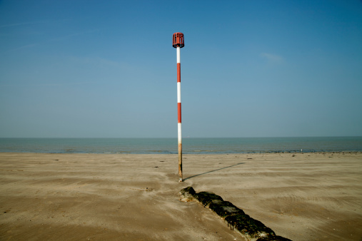 A tall red and white striped warning post on a sunny beach.
