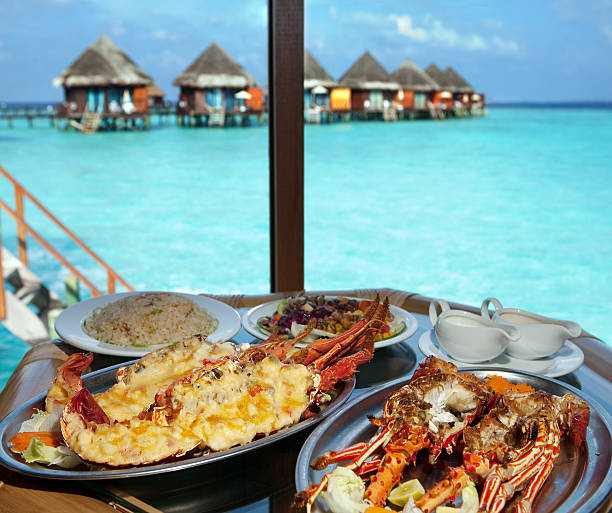 Two plates with lobster on table at window Two plates with lobster on table at window with view on ocean maldivian culture stock pictures, royalty-free photos & images