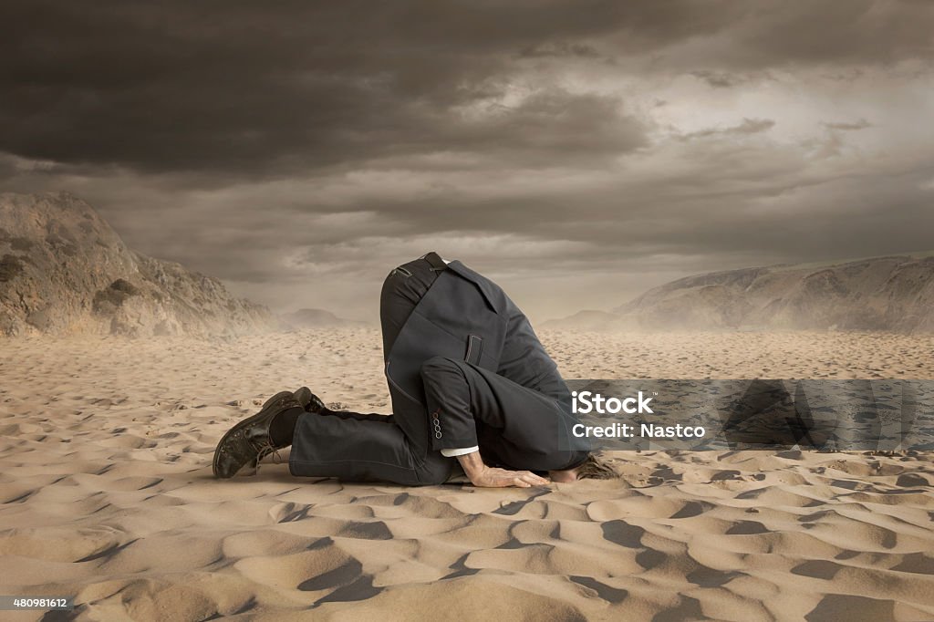 Crisis Young businessman hiding head in the sand Head in the Sand Stock Photo