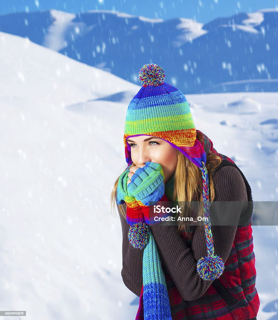 Female in winter mountains Picture of cute female in winter mountains, snowfall outdoors, beautiful woman wearing colorful wool hat, scarf and gloves, woman froze outdoor in cold snowy weather, wintertime holidays Adult Stock Photo