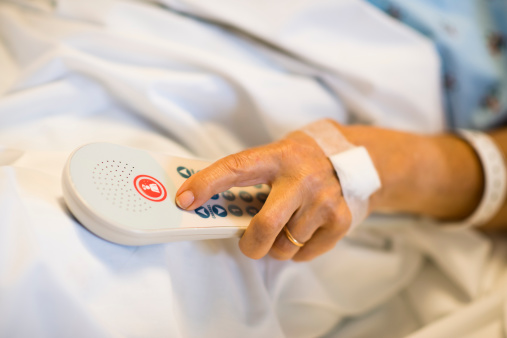 Elderly woman's hand with call button in a hospital bed.