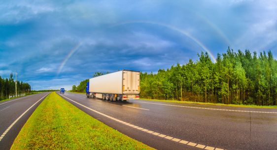 Truck on the highway after the rain driving under the rainbow