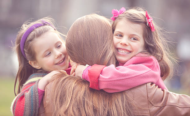 Two Happy Daughters Embracing their Mother Two Happy Daughters Embracing their Mother in the Spring Day . three way kiss stock pictures, royalty-free photos & images
