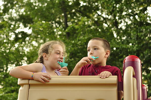 istock Young Boy and Girl Eating Popsicles at Playground 481010512