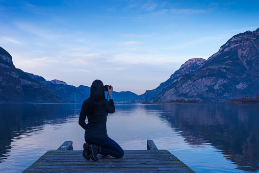 Young woman with a camera on the lake at sunset. Landscape photographer
