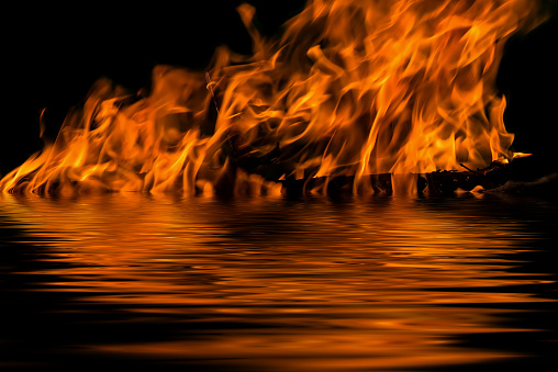 The flames from the fire on a black background with reflection in water